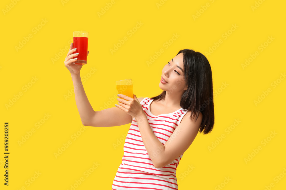 Beautiful Asian woman with glasses of juice on yellow background Beautiful Asian woman with glasses of juice on yellow background