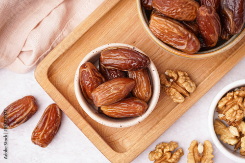 Bowls with dried dates and nuts on light background