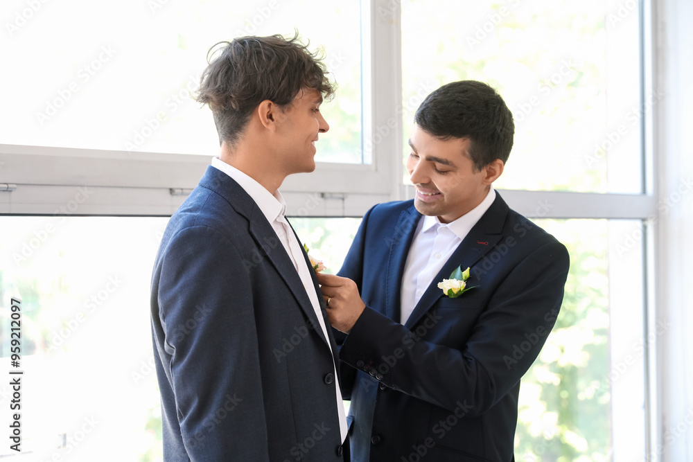 Young man fixing his husband's boutonniere on their wedding day Young man fixing his husband's boutonniere on their wedding day