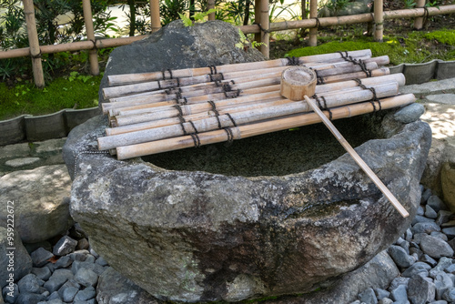 A traditional Japanese stone basin, Tsukubai, or stooping basin, filled with low wash water and a bamboo ladle, commonly found in classical Japanese tea gardens, temples, and shrines. photo