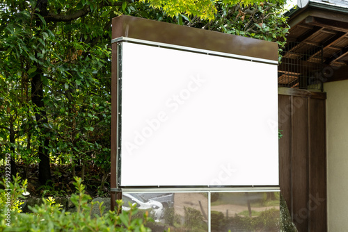 Blank white mockup background texture of a rectangular billboard in a Japanese garden,surrounded by lush trees and plants, with a low stone wall. Information or guidance board to display a map in park photo