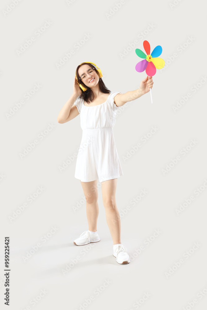 Young woman in headphones with toy windmill on light background Young woman in headphones with toy windmill on light background