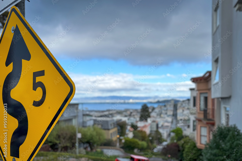 Traffic sign allowing speed of 5 mph due to winding road at Lombard Street against blue sky with blurred cityscape of San Francisco, California, USA Traffic sign allowing speed of 5 mph due to winding road at Lombard Street against blue sky with blurred cityscape of San Francisco, California, USA