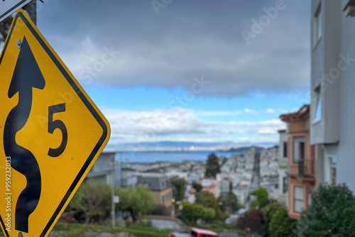 Traffic sign allowing speed of 5 mph due to winding road at Lombard Street against blue sky with blurred cityscape of San Francisco, California, USA