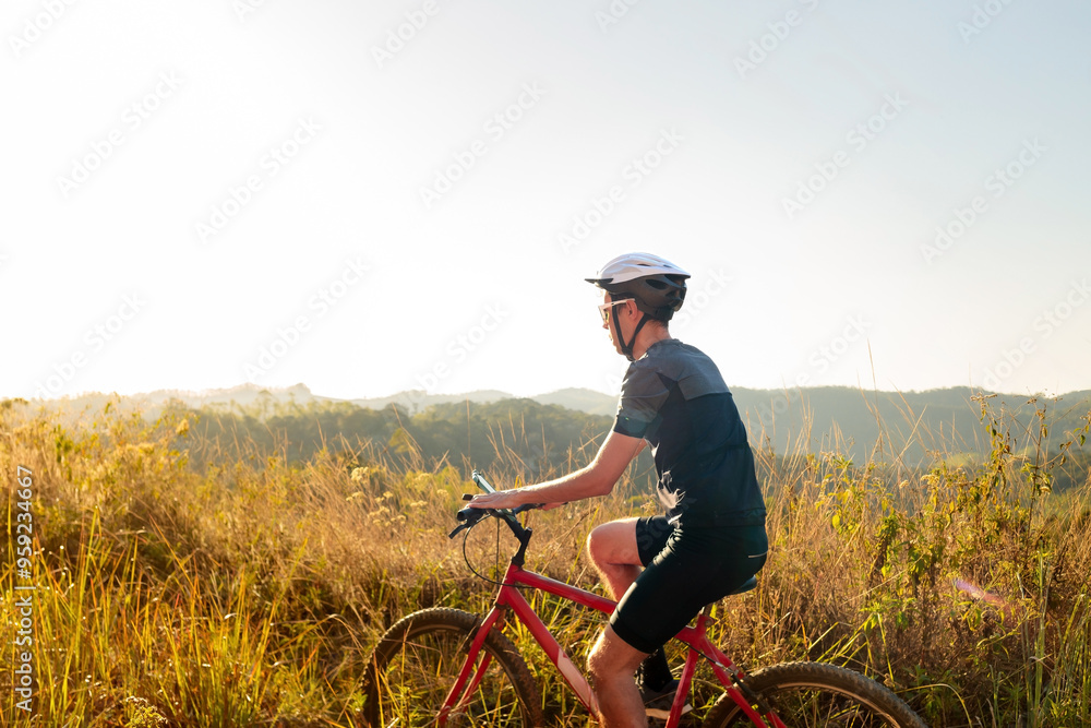 Obraz premium Cyclist riding a bike on a trail on a sunny day. He is wearing cycling gear and apparel. Inspirational image of a healthy lifestyle through cycling