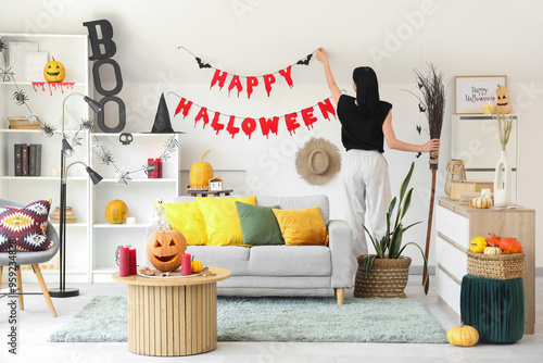 Woman hanging Halloween garland on light wall at home, back view