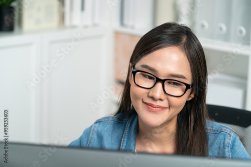 Working young beautiful asian creative manager with glasses focusing on pc, creating with new website design on social media online planning with blue jeans shirt at modern home office. Stratagem.