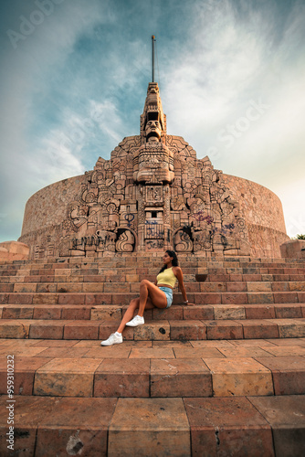 Mujer latina hermosa, de cabello rizado, sentada en las escaleras del monumento a la Patria, disfrutando de la vista al amanecer, en Mérida Yucatán, México photo