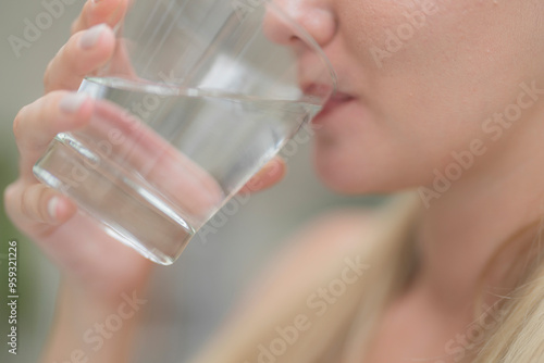 A beautiful European woman smiles happily, holding a glass of water, drinking natural mineral water from a clear glass, inside a residential. A healthy woman shows her face, complete physical health.