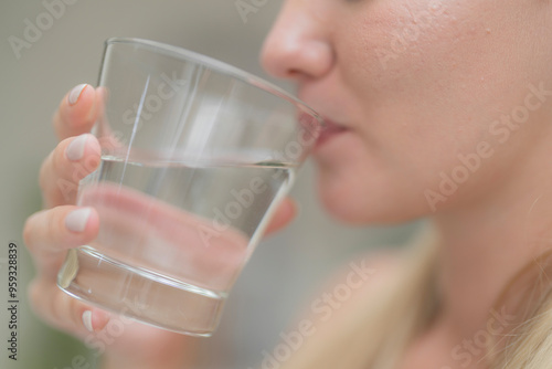 A beautiful European woman smiles happily, holding a glass of water, drinking natural mineral water from a clear glass, inside a residential. A healthy woman shows her face, complete physical health.