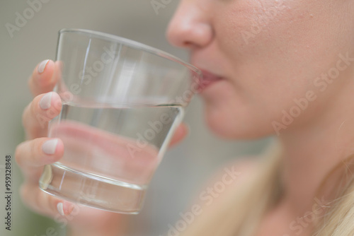 A beautiful European woman smiles happily, holding a glass of water, drinking natural mineral water from a clear glass, inside a residential. A healthy woman shows her face, complete physical health.