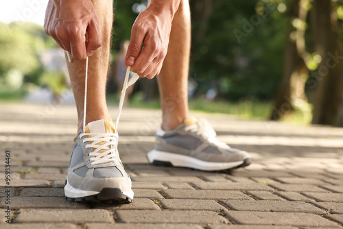 Man tying shoelace of grey sneaker outdoors, closeup. Space for text