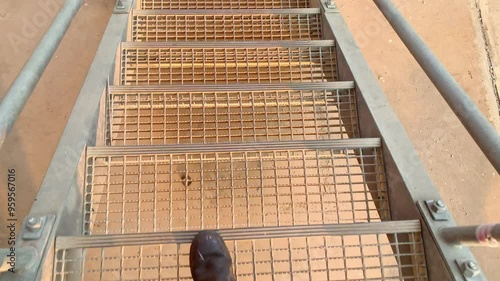 Metal Stairs Leading Upwards. A person walking up a set of metal stairs, the view from the top of the stairs shows a grated platform