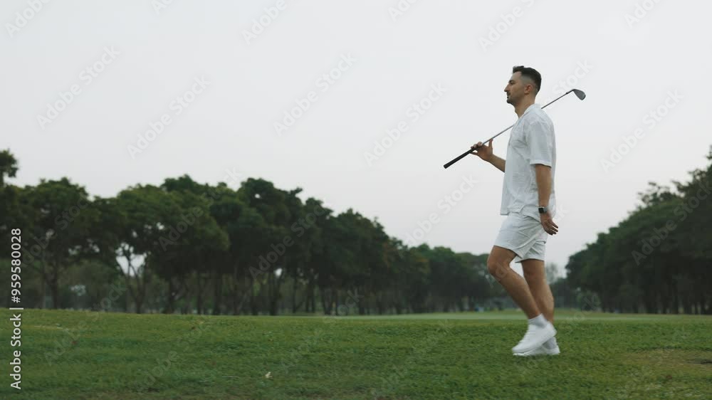 Relaxed man with golf club walking along green sports field full length portrait. Skilled athlete with iron driver trains on summer course. Sportive guy exercises on lawn grass Relaxed man with golf club walking along green sports field full length portrait. Skilled athlete with iron driver trains on summer course. Sportive guy exercises on lawn grass