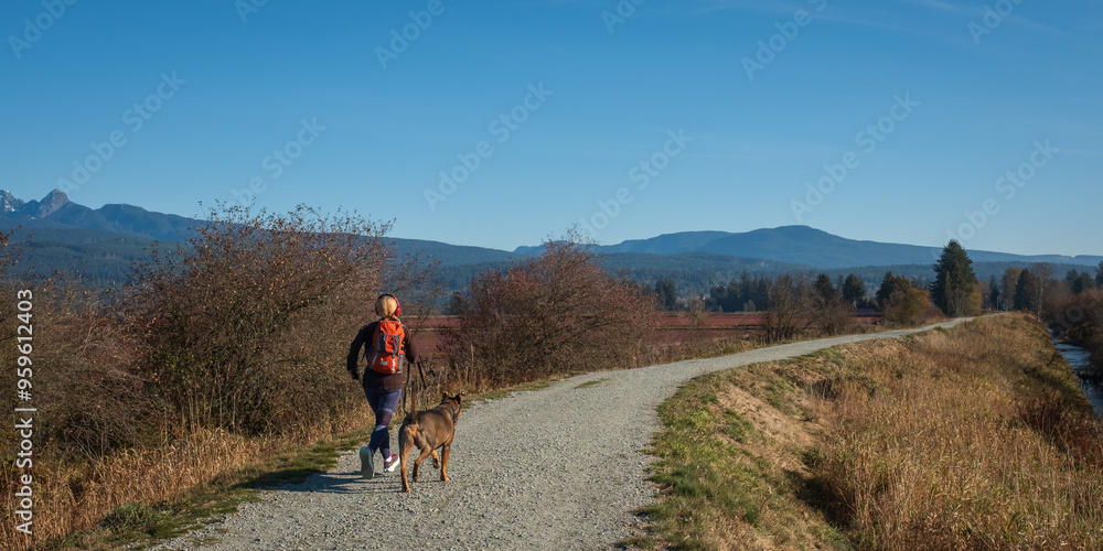 Picture from behind of a Blonde girl running in the nature with her dog on her side. Fitness, outdoor Sports. Picture from behind of a Blonde girl running in the nature with her dog on her side. Fitness, outdoor Sports.