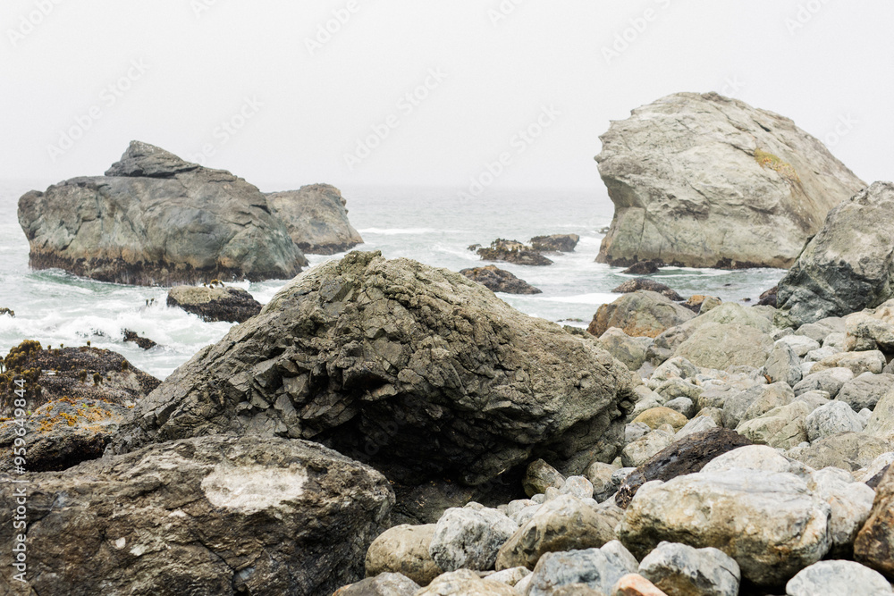Large rocks along a foggy coastline with waves and an overcast sky Large rocks along a foggy coastline with waves and an overcast sky