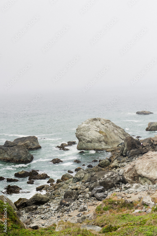 Foggy coastal rocks and calm ocean waves under an overcast sky Foggy coastal rocks and calm ocean waves under an overcast sky