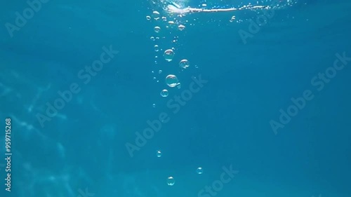 Slow-motion underwater footage of bubbles rising to the surface in a turquoise, crystal-clear pool, capturing their gentle ascent and delicate movements in the pristine water