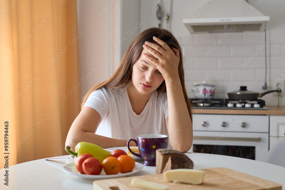 Distraught depressed Caucasian woman sitting at table in kitchen with leaning head on her hand looking at simple meal with sadness in her facial expression having no appetite Distraught depressed Caucasian woman sitting at table in kitchen with leaning head on her hand looking at simple meal with sadness in her facial expression having no appetite