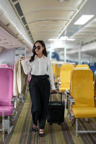 Asian businesswoman dragging a suitcase Walking the airplane aisle to find her seat on a domestic business trip. Online work. Business travel concept.