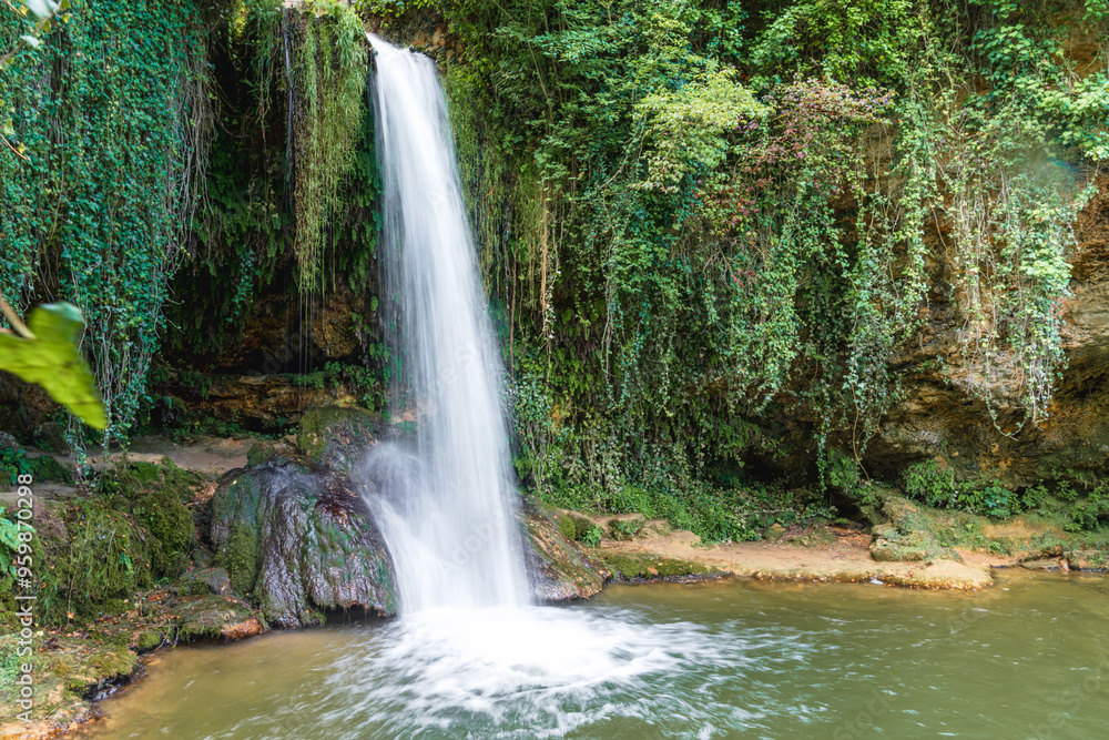 A serene waterfall cascades over rocks into a tranquil pool surrounded by lush greenery in a peaceful outdoor setting A serene waterfall cascades over rocks into a tranquil pool surrounded by lush greenery in a peaceful outdoor setting