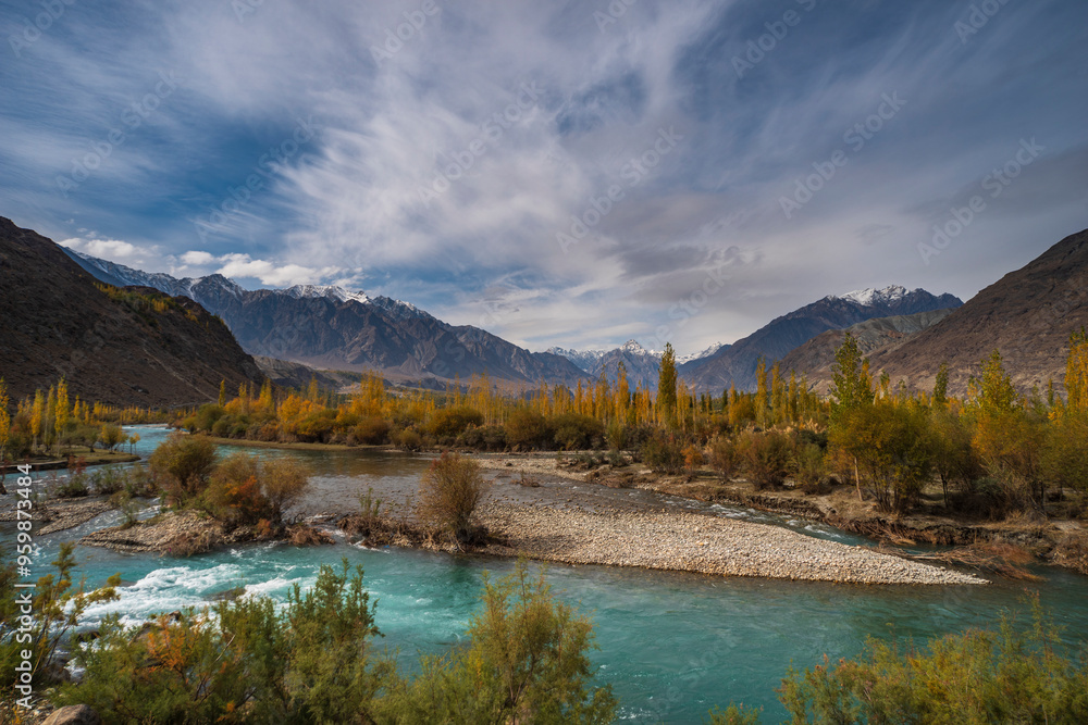 View of the majestic Gilgit River winding through a picturesque valley surrounded by rugged mountains and lush trees, Ghizer, Pakistan.
