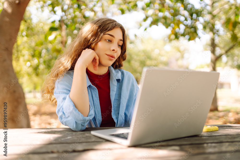 Young freelancer woman in casual attire focused on laptop while sitting at a park table on a sunny day, enjoying a moment of productivity. E-learning concept. Remote work. Young freelancer woman in casual attire focused on laptop while sitting at a park table on a sunny day, enjoying a moment of productivity. E-learning concept. Remote work.