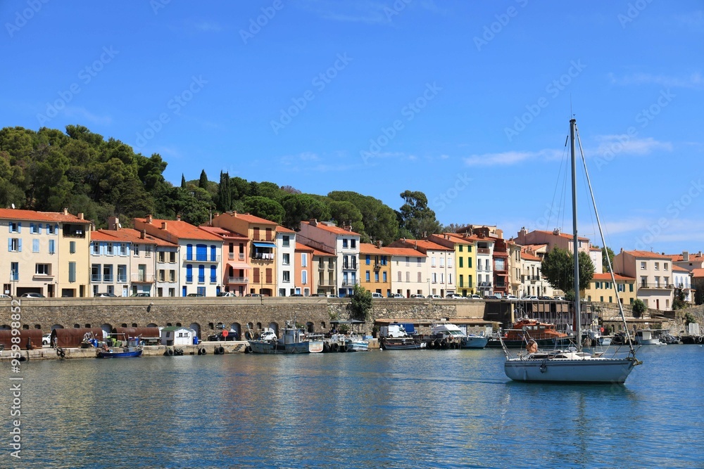 Sailboat in harbour against backdrop of colourful house fronts and blue sky in Mediterranean port town of Port-Vendres, Pyrénées-Orientales department, southern France Sailboat in harbour against backdrop of colourful house fronts and blue sky in Mediterranean port town of Port-Vendres, Pyrénées-Orientales department, southern France