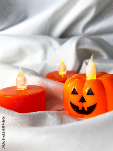 Orange battery powered candles in the shape of a pumpkin on a white textile background. Top view.