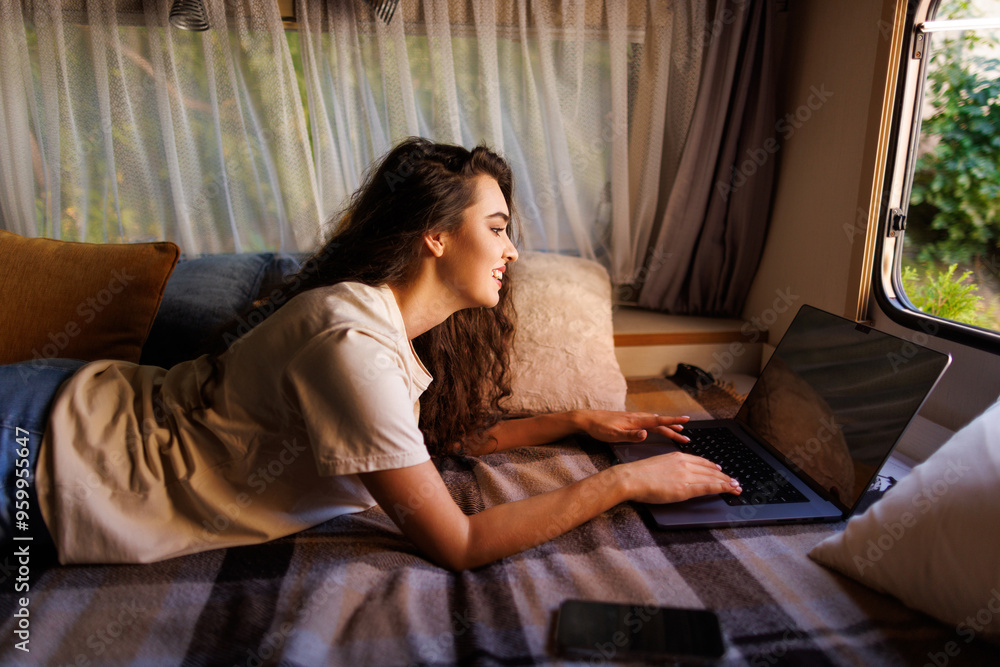 Woman lying face down on the bed of her camper van while working remotely with her laptop Woman lying face down on the bed of her camper van while working remotely with her laptop