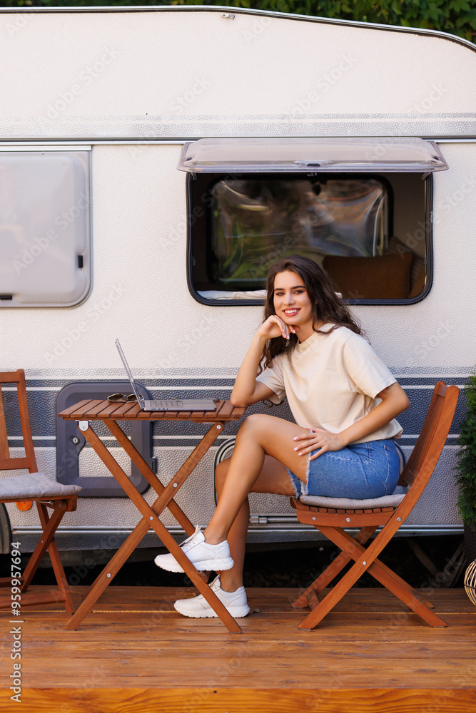 Camper life. Young woman sitting on chairs and picnic table with her camper housing behind, in the countryside. Camper life. Young woman sitting on chairs and picnic table with her camper housing behind, in the countryside.