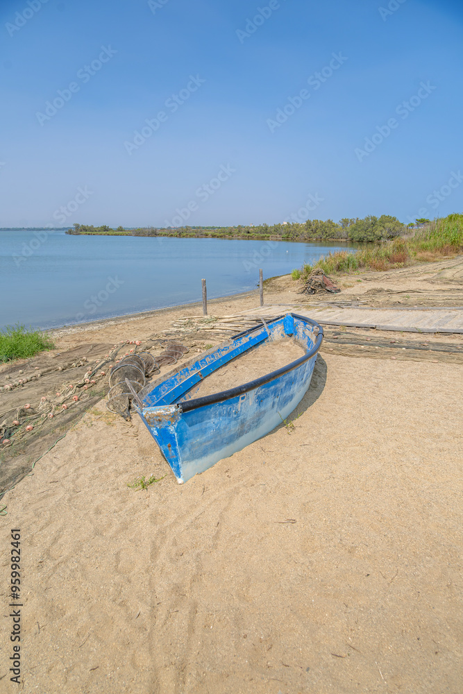 Old Blue Wooden Fishing Boat Abandoned On The Sandy Shore Next To Nets And Traps On A Lake Beach And Vegetation In The Distance, A Sunny Day With Natural Scenery At Canet-saint-nazaire Lagoon (éTang) Old Blue Wooden Fishing Boat Abandoned On The Sandy Shore Next To Nets And Traps On A Lake Beach And Vegetation In The Distance, A Sunny Day With Natural Scenery At Canet-saint-nazaire Lagoon (éTang)