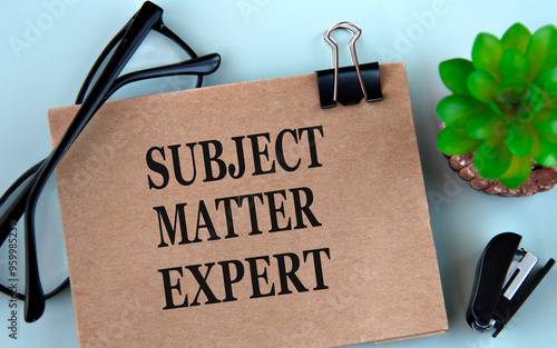 SUBJECT MATTER EXPERT - words on brown paper on a light background with glasses, cactus and stapler
