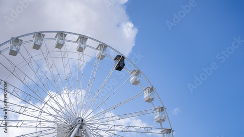 Partial view of a ferris wheel with the white cabins and one black in an amusement park against a clear blue sky
