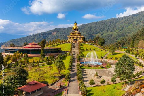 Ravangla Buddha Park, Sikkim, India, with a large golden Buddha statue, green hills, blue sky, and landscaped gardens. The park’s serene environment and pathways make it a cultural landmark