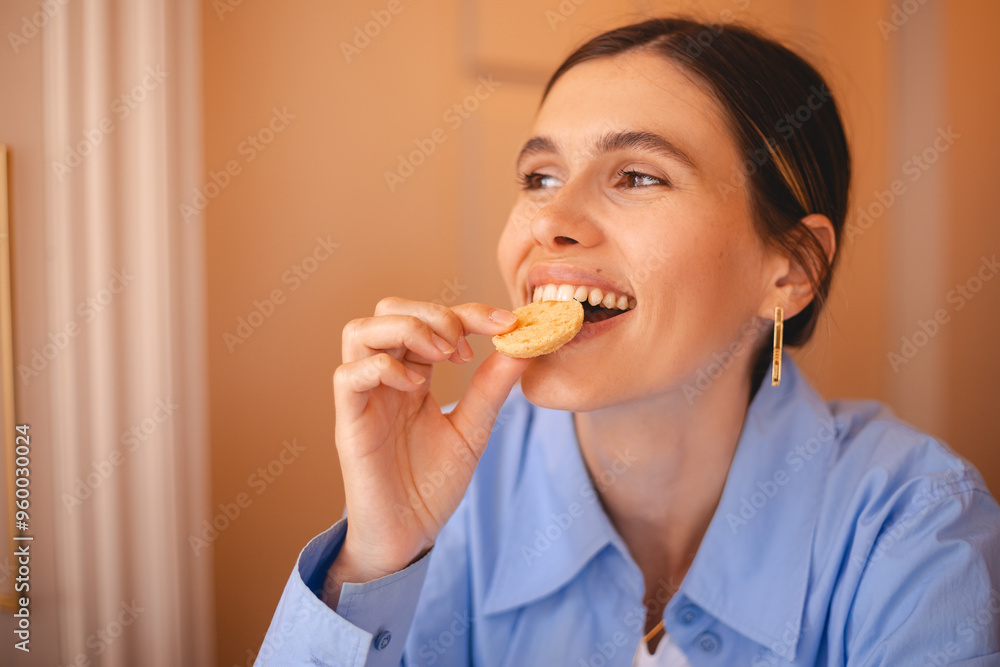 Happy woman eating cookie sitting in a restaurant. Positive woman bites cookie enjoys eating sweet food breaks diet. Woman wear blue shirt, low ponytail rest in cafe. Girl bite cake and look happy. Happy woman eating cookie sitting in a restaurant. Positive woman bites cookie enjoys eating sweet food breaks diet. Woman wear blue shirt, low ponytail rest in cafe. Girl bite cake and look happy.