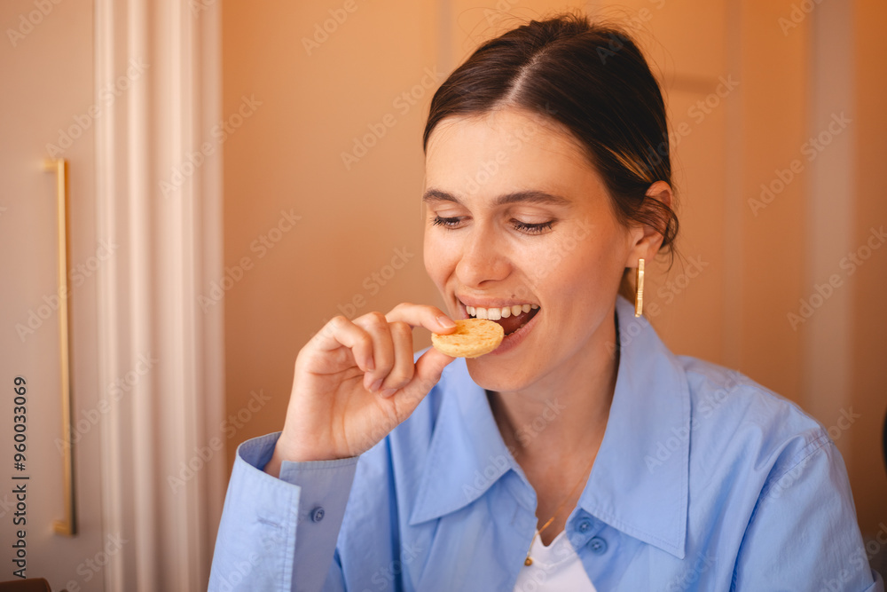 Happy woman eating cookie sitting in a restaurant. Positive woman bites cookie enjoys eating sweet food breaks diet. Woman wear blue shirt, low ponytail rest in cafe. Girl bite cake and look happy. Happy woman eating cookie sitting in a restaurant. Positive woman bites cookie enjoys eating sweet food breaks diet. Woman wear blue shirt, low ponytail rest in cafe. Girl bite cake and look happy.