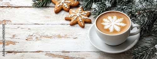 Cup of coffee with snowflake latte art beside gingerbread cookies and frosted pine branches on a snow-dusted wooden surface