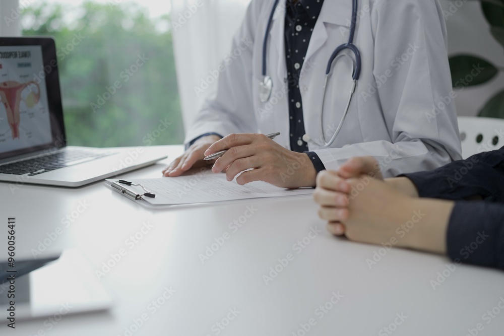 Doctor and a patient are sitting at the white table in clinic. The female physician is using clipboard for making notes during a consultation, close up of woman hands. Medicine concept Doctor and a patient are sitting at the white table in clinic. The female physician is using clipboard for making notes during a consultation, close up of woman hands. Medicine concept