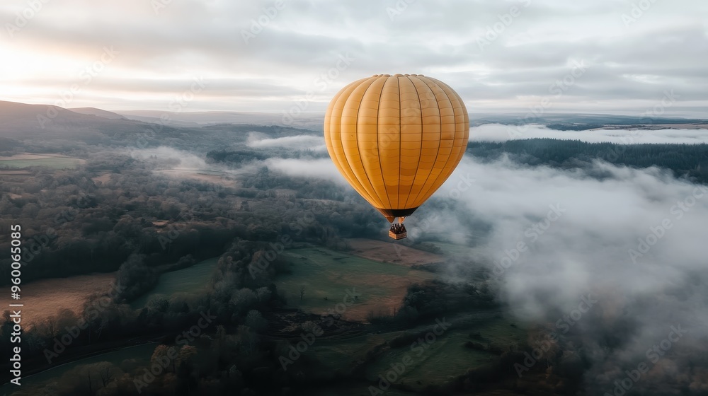 Fototapeta premium A vibrant yellow hot air balloon floats high in the misty sky, offering a stunning aerial view of the expansive, peaceful landscape and symbolizing adventure and freedom.