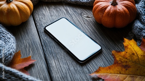 Blank smartphone screen with autumn leaves, pumpkins, and a cozy sweater on wooden surface