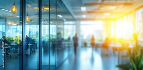 Blurred office interior with blurred people working in the background and a glass door leading to a modern business space with sunlight