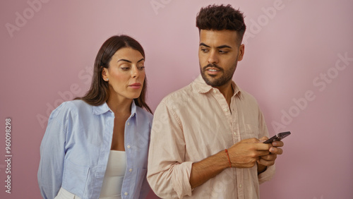 Obraz na plátně Woman spying on man using mobile phone against pink wall, showcasing relationshi