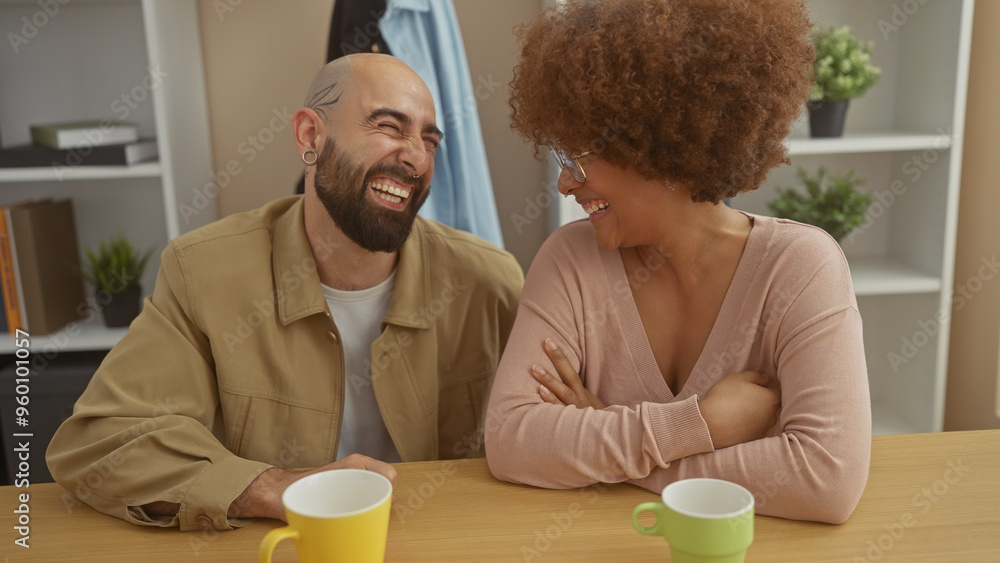 A laughing interracial couple enjoying a casual indoor setting with coffee cups on the table. A laughing interracial couple enjoying a casual indoor setting with coffee cups on the table.