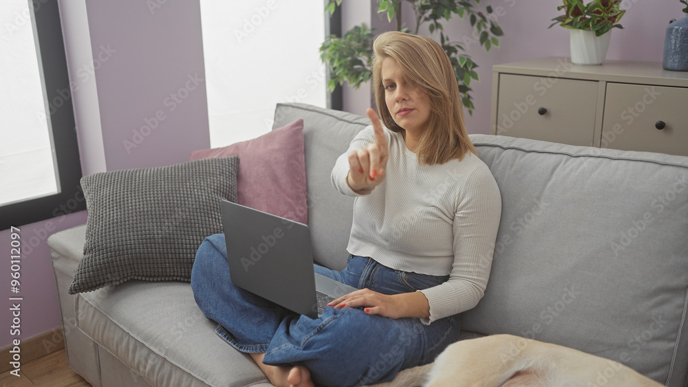A young woman gestures no while sitting with a laptop on a couch in a cozy living room setting. A young woman gestures no while sitting with a laptop on a couch in a cozy living room setting.