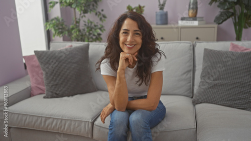 A smiling middle-aged brunette woman sitting comfortably on a couch in a modern living room interior