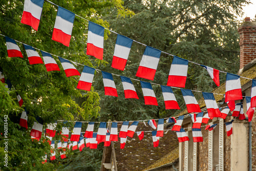 Fototapeta Naklejka Na Ścianę i Meble -  Arrangements de guirlandes de drapeaux tricolores décorant la rue d'un village en France avec des arbres à l'arrière plan. Concepts de fête nationale et d'évènement festif ou patriotique français