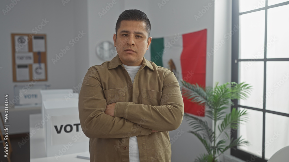 Hispanic man with arms crossed standing in a voting room with mexico flag indoors Hispanic man with arms crossed standing in a voting room with mexico flag indoors