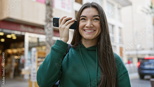 Wallpaper Mural Smiling young hispanic woman holding a smartphone on an urban street. Torontodigital.ca