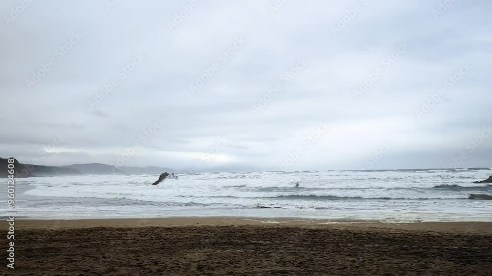 A cloudy day at Sopelana beach with crashing waves, rugged cliffs, dark skies, and a calm, windy, and moody atmosphere A cloudy day at Sopelana beach with crashing waves, rugged cliffs, dark skies, and a calm, windy, and moody atmosphere